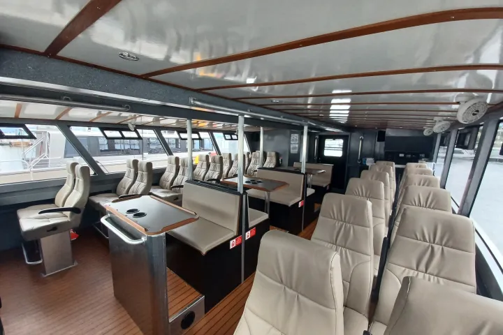 Interior of a modern ferry with rows of beige seats and large windows on both sides.
