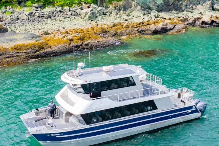 A boat cruises on turquoise water near a rocky, forested shoreline.