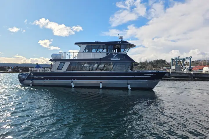 A modern, multi-deck tour boat on calm water with a blue sky and some clouds in the background.